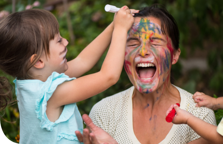 Child drawing on woman's face with colorful markers