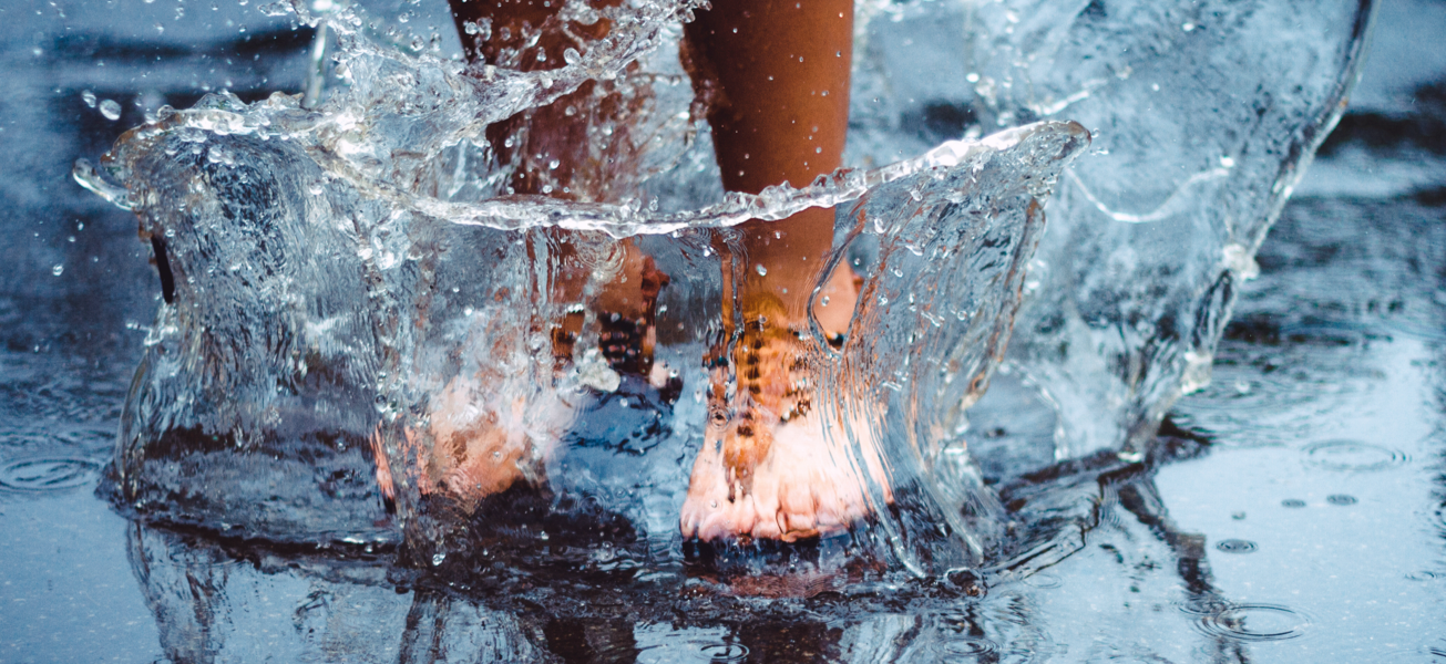 Bare feet splashing in water puddle