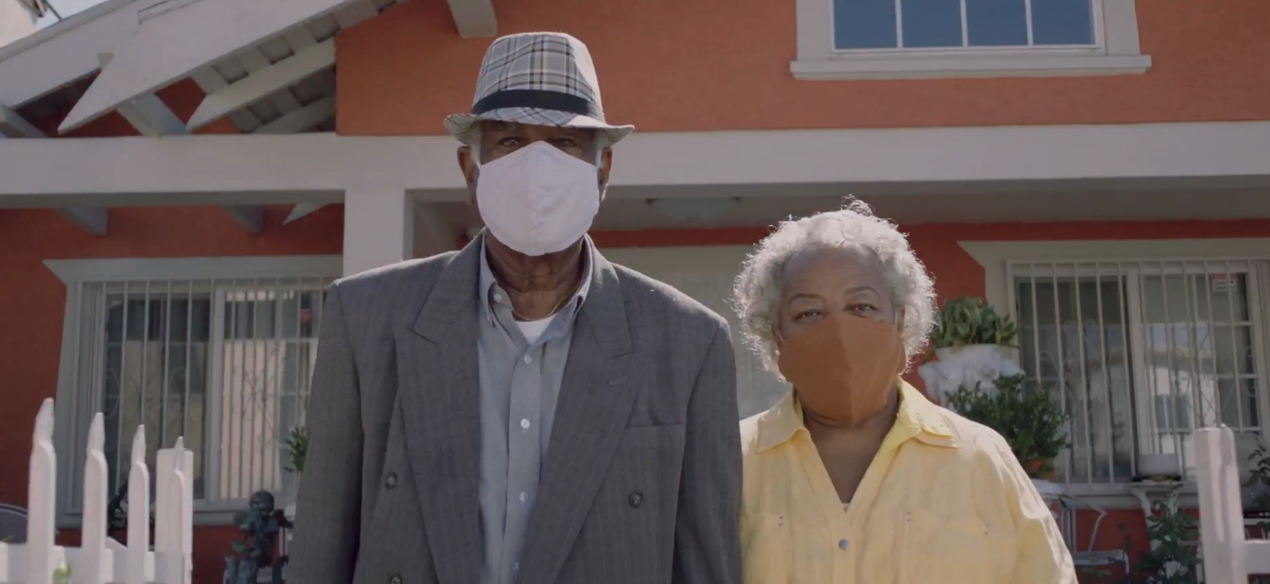 Old couple wearing masks standing in front of house