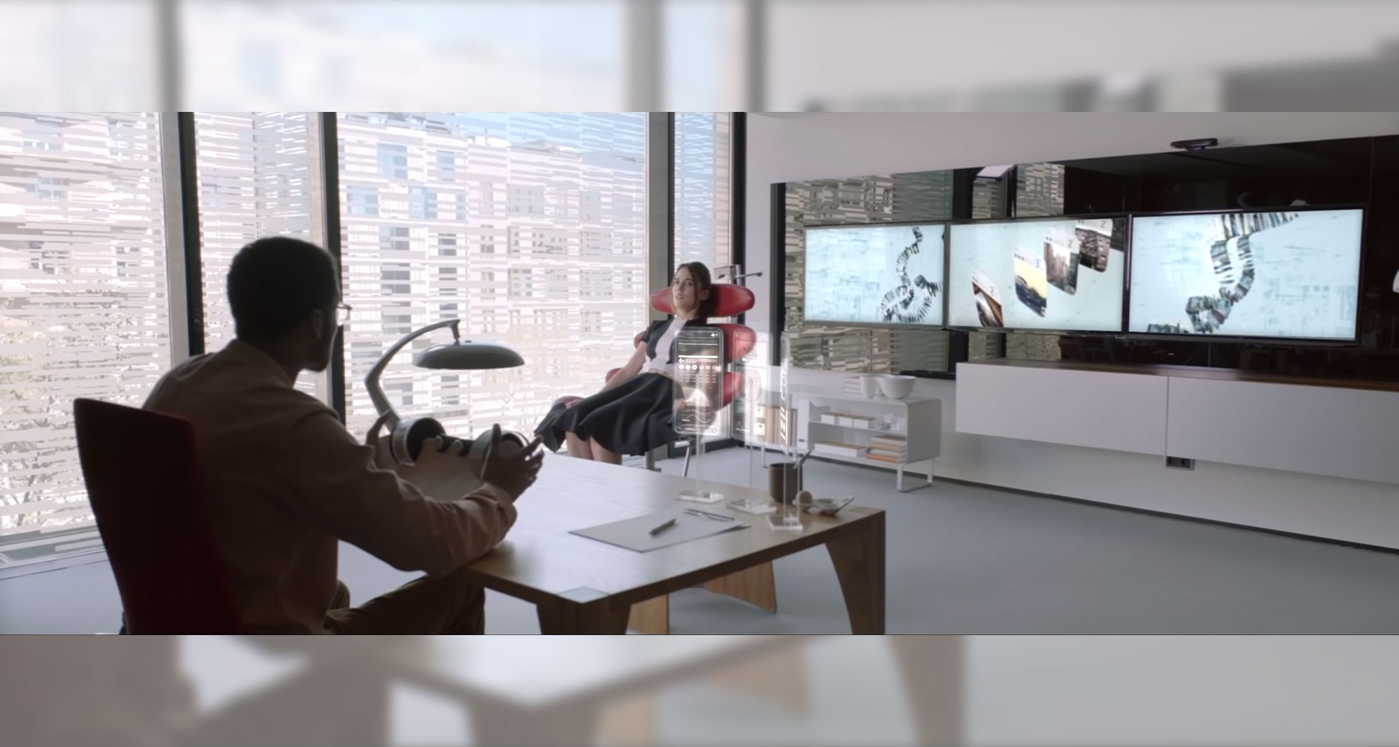 Beyond Money short film screenshot: Man and woman in sunlit office with three large computer screens