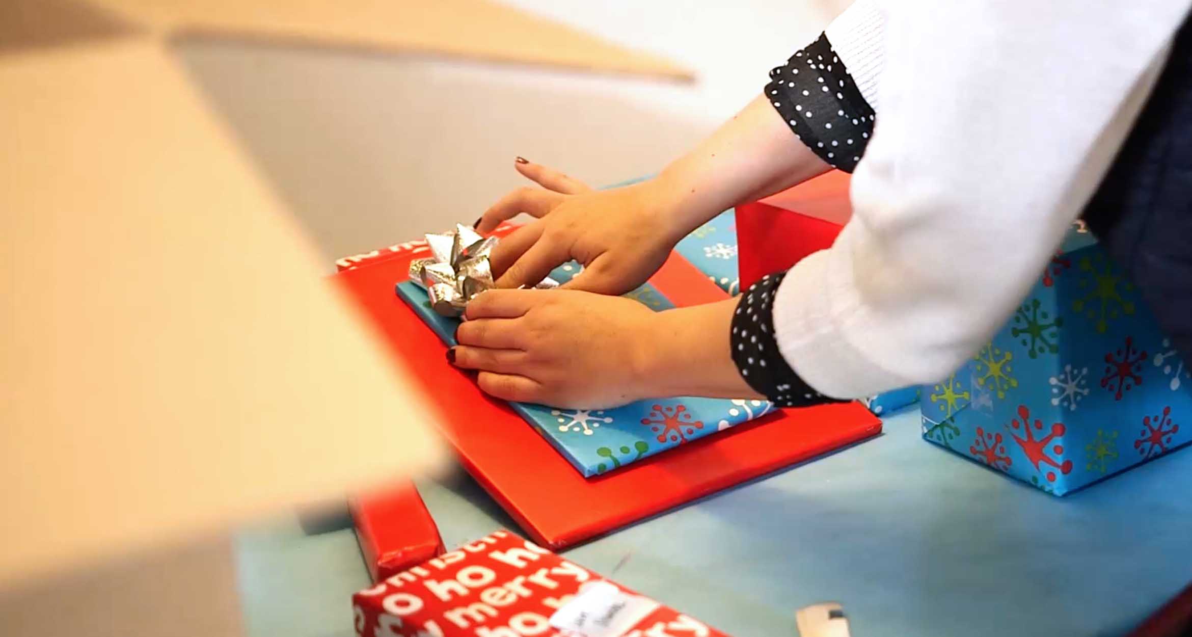 Person wrapping a gift in holiday paper 